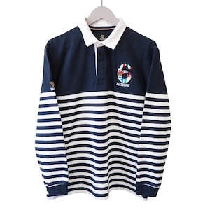 May include: Navy blue and white striped long-sleeve rugby shirt. The shirt features a white collar and a button-down placket. The number "6" is embroidered on the chest, along with the word "NATIONS". The shirt is hanging on a wooden hanger.