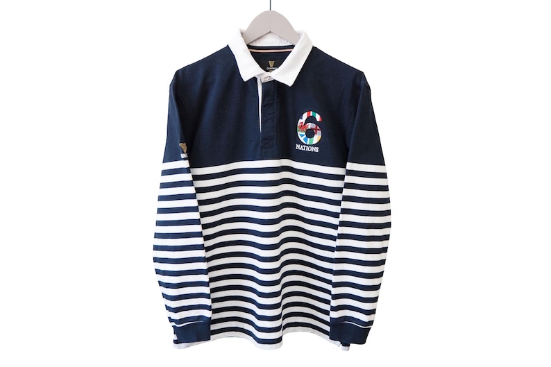 May include: Navy blue and white striped long-sleeve rugby shirt. The shirt features a white collar and a button-down placket. The number "6" is embroidered on the chest, along with the word "NATIONS". The shirt is hanging on a wooden hanger.