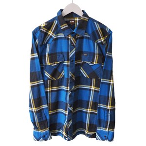May include: A blue, black, and yellow checked shirt with long sleeves. The shirt has two chest pockets and a button-down collar. It is hanging on a white hanger.