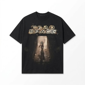 May include: Black t-shirt featuring the text "DEAD SPACE" in a glowing, distressed font above an image of a figure in a dark corridor. The figure is holding a weapon. The shirt has short sleeves and a crew neck.