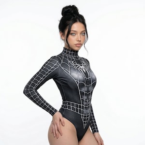 Może przedstawiać: Czarny i szary body z pajęczyną i pająkiem. Body z długim rękawem ma wysoki dekolt i dopasowaną sylwetkę. Wzór pająka znajduje się na klatce piersiowej i plecach. Body jest wykonane z elastycznego materiału.