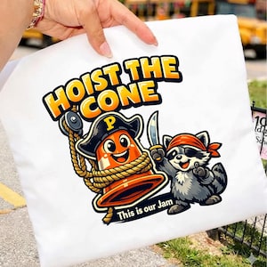 Peut inclure: Taie d'oreiller blanche avec un dessin anim&eacute; d'un c&ocirc;ne de signalisation pirate et d'un raton laveur pirate, avec le texte "HOIST THE CONE" et "This is our Jam". Le c&ocirc;ne est orange et le raton laveur est gris.