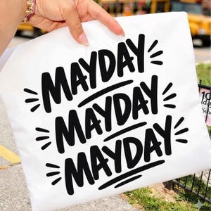 Peut inclure: Taie d'oreiller blanche avec le mot "MAYDAY" en lettres noires grasses, répété trois fois. Chaque mot est souligné et comporte trois petites lignes rayonnant de chaque côté.