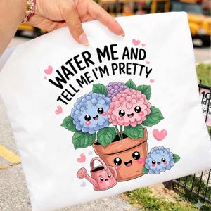 Puede incluir: Funda de almohada blanca con una ilustración de dibujos animados de hortensias en una maceta, una regadera y el texto "WATER ME AND TELL ME I'M PRETTY". Las flores son azules, rosas y moradas.