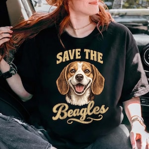 May include: Black crew neck t-shirt featuring a smiling beagle illustration with the text "SAVE THE Beagles" in a vintage style font. The beagle has brown and white fur. The shirt is a comfortable, casual style.