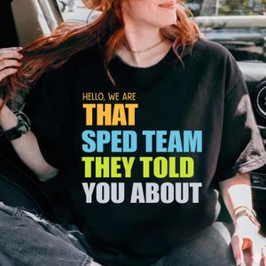 Puede incluir: Camiseta negra con el texto "HELLO, WE ARE THAT SPED TEAM THEY TOLD YOU ABOUT" en amarillo, azul, verde y blanco. La camiseta la lleva una persona con cabello castaño rojizo.