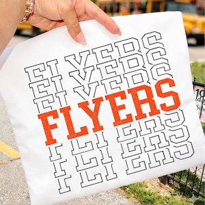 Puede incluir: Un cojín cuadrado blanco con la palabra "FLYERS" en letras grandes de color naranja. La palabra está rodeada por la palabra "FLYERS" en un patrón repetitivo en letras negras. El cojín está sostenido por una persona.