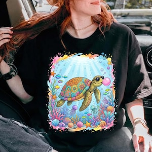 Puede incluir: Camiseta negra con un gráfico de dibujos animados colorido de una tortuga marina con gafas de sol soplando una burbuja. La tortuga está rodeada de corales, peces y burbujas. El diseño tiene un estilo vibrante y de dibujos animados.
