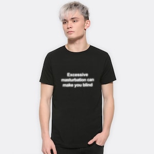May include: Black t-shirt with the text "Excessive masturbation can make you blind" in a white, glowing font. The shirt is short-sleeved and appears to be made of a soft material. The shirt is being worn by a person.