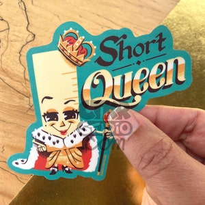 May include: A teal blue sticker with a cartoon ruler wearing a gold crown and a red and gold robe. The ruler is holding a scepter and has a smiling face. The text "Short Queen" is written in a stylized font above the ruler.