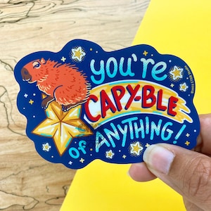 May include: A blue and yellow sticker with a cartoon capybara sitting on a gold star. The sticker says "You're Capy-ble of Anything!"