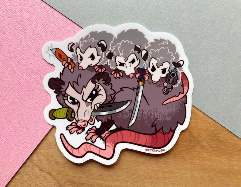 Peut inclure: Un autocollant repr&eacute;sentant une illustration de dessin anim&eacute; d'un opossum avec trois b&eacute;b&eacute;s opossums. L'opossum tient un couteau et les b&eacute;b&eacute;s opossums tiennent des armes. L'autocollant est blanc avec un sch&eacute;ma de couleurs rouge, gris et brun.