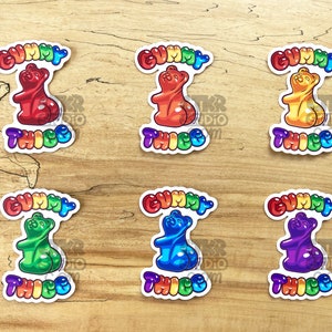 May include: Six colorful gummy bear stickers with the text "Gummy Thicc" in rainbow letters. The gummy bears are red, orange, yellow, green, blue, and purple.