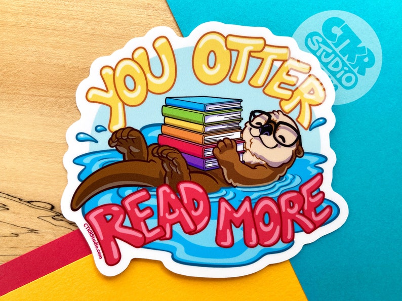 May include: A sticker featuring a cartoon otter wearing glasses and holding a stack of colorful books. The otter is floating in blue water with the text "You Otter Read More" in pink and yellow letters.