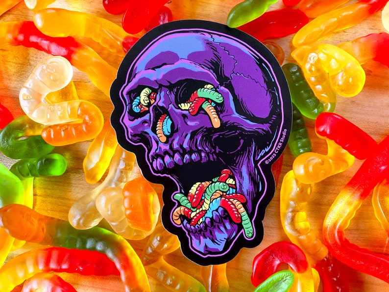 May include: Purple skull sticker with a black background. The skull's eyes and mouth are filled with colorful gummy worms. The sticker has the text "&copy;2021 CTR Studio" in the lower right corner.