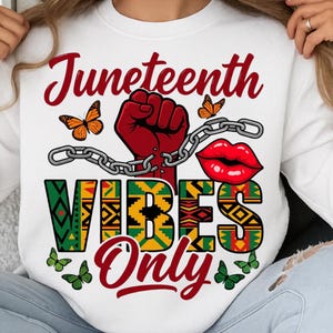 May include: White sweatshirt with a graphic design featuring the word "Juneteenth" in red script, a red fist, a chain, red lips, and the words "Vibes Only." The design includes butterflies and patterns in green, yellow, and black.