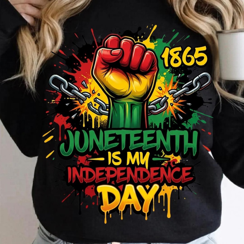May include: Black long-sleeve shirt with a graphic celebrating Juneteenth. The design features a raised fist in red, yellow, and green, breaking chains. The text reads "Juneteenth is my Independence Day" with the year 1865.