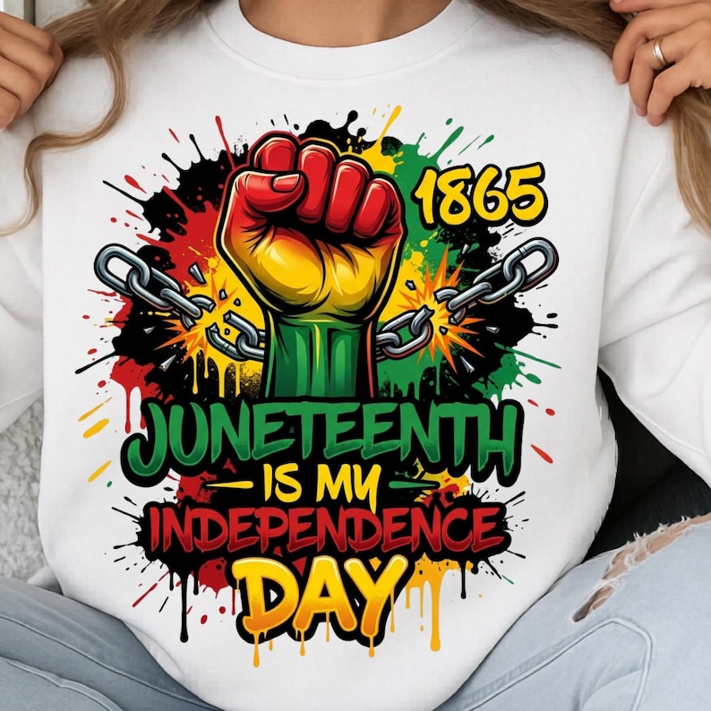 May include: White sweatshirt with a colorful graphic celebrating Juneteenth. The design features a raised fist in red, yellow, and green, chains, the year 1865, and the text "Juneteenth is my Independence Day."