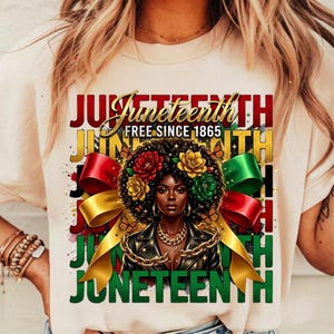 May include: A cream-colored t-shirt featuring a graphic celebrating Juneteenth. The design includes the word "Juneteenth" in multiple colors, a portrait of a woman with floral hair, and the text "FREE SINCE 1865". Ribbons and butterflies are also included.