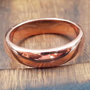 Puede incluir: Un anillo de cobre pulido con una banda lisa y redondeada. El anillo refleja la luz, mostrando su cálido color marrón rojizo. El anillo es de diseño simple y clásico, adecuado para el uso diario.