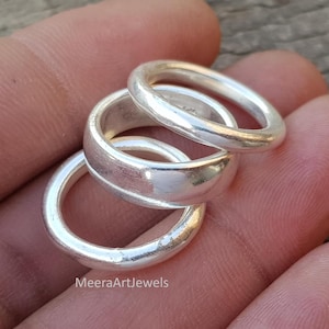 May include: Three silver rings stacked together, showcasing a minimalist design. The rings are smooth and shiny, reflecting light. The rings are likely made of sterling silver. The rings are a simple and elegant accessory.