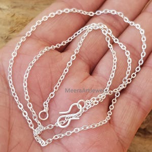 Puede incluir: Un delicado collar de cadena de plata con un diseño de eslabones ovalados. El collar presenta un cierre de mosquetón. La cadena se muestra sobre un fondo neutro. El collar es una joya.