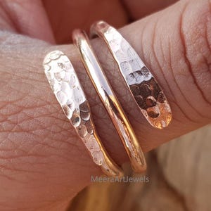 May include: A rose gold spiral ring with a hammered texture. The ring wraps around the finger, featuring three bands. The ring is a warm, metallic color and reflects light. The ring is a piece of jewelry.