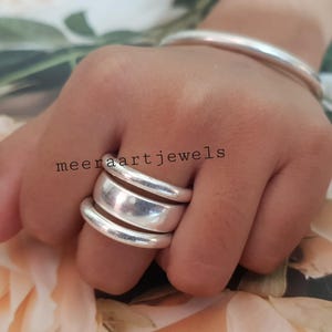 May include: A hand adorned with a stackable silver ring and a silver bangle. The ring features three bands of different widths. The text "meeraartjewels" is visible on the hand.