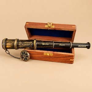 Peut inclure: Un télescope en laiton et métal sombre avec une boussole attachée par une chaîne, portant les inscriptions gravées DOLLOND LONDON et To the brave Bassoon. Le télescope repose dans une boîte en bois rectangulaire ouverte avec un intérieur bleu.