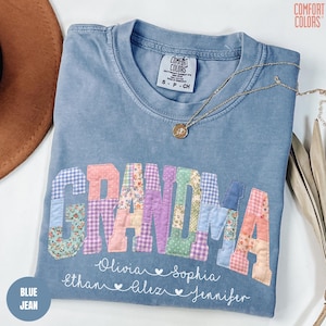 May include: A blue jean Comfort Colors t-shirt with the word "GRANDMA" in patchwork letters. The names Olivia, Ethan, Sophia, Aliz, and Jennifer are written below the word "GRANDMA". A gold necklace is draped across the shirt.