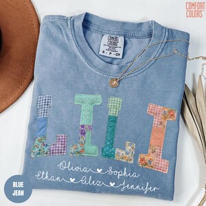 May include: Blue jean Comfort Colors t-shirt with the letters "LILI" appliqued in various patterned fabrics. Below the letters are names, including Olivia, Sophia, Ethan, and Jennifer. A gold necklace rests on the shirt.