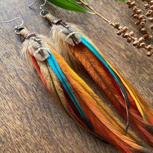 May include: A pair of long, colorful feather earrings with turquoise accents. The earrings are made with natural feathers and have a leather wrap at the top.
