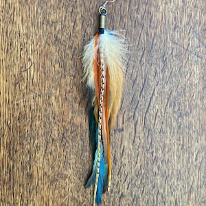 Puede incluir: Un pendiente largo de plumas multicolores con un gancho dorado. Las plumas son marrones, beige, blancas y azules.