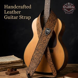 May include: Handcrafted leather guitar strap with a floral embossed design in brown and black, draped over an acoustic guitar. The strap features the text "P&P music" on a shield-shaped patch.