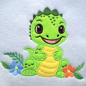 May include: Embroidered patch featuring a smiling green dinosaur with a yellow belly, surrounded by blue and orange flowers and green leaves. The dinosaur has large brown eyes and a pink mouth. The patch is on a white background.
