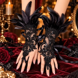 May include: A pair of black fingerless gloves featuring intricate lace embroidery, small sequins, and black feathers at the wrist. The gloves include thin black ribbons for tying and a loop that secures around the middle finger, covering the back of the hand.