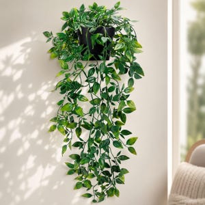 May include: A wall-mounted black planter containing a trailing artificial plant with numerous pointed green leaves. The foliage cascades downwards from the container, displaying various shades of green with light-coloured veins on the surface of the leaves.