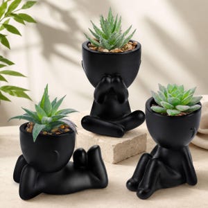 Puede incluir: Tres macetas de cerámica negra con forma de figuras humanas en diferentes poses. Cada maceta contiene una planta suculenta con hojas verdes y pequeñas piedras. Las macetas están sobre un fondo neutro.