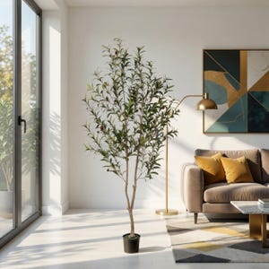 May include: A tall artificial olive tree in a black pot. The tree has green leaves and small, dark-colored fruit. It stands in a bright, modern living room with a sofa, rug, and artwork. The tree is a decorative element.