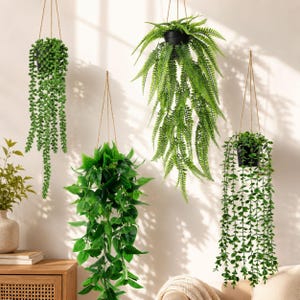 May include: Four artificial hanging plants in black pots suspended by thin ropes. The collection includes a string of pearls, a lush fern, a broad-leafed trailing plant, and a vine with small round leaves, all featuring vibrant green foliage.