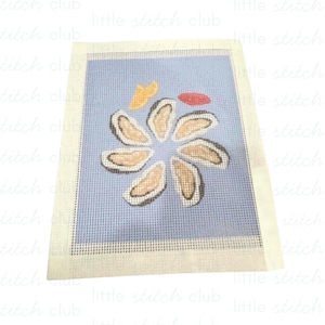May include: A needlepoint canvas featuring a light blue background with a circular arrangement of six oyster shells in shades of tan and brown. Above the oysters are a small yellow lemon wedge and a small red dollop of cocktail sauce.