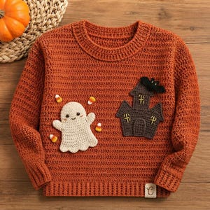 May include: A long-sleeve orange crochet sweater featuring a white ghost appliqué, a dark brown haunted house appliqué with a black bat on top, and small yellow and orange candy corn accents. The sweater has a ribbed crew neckline and hem.