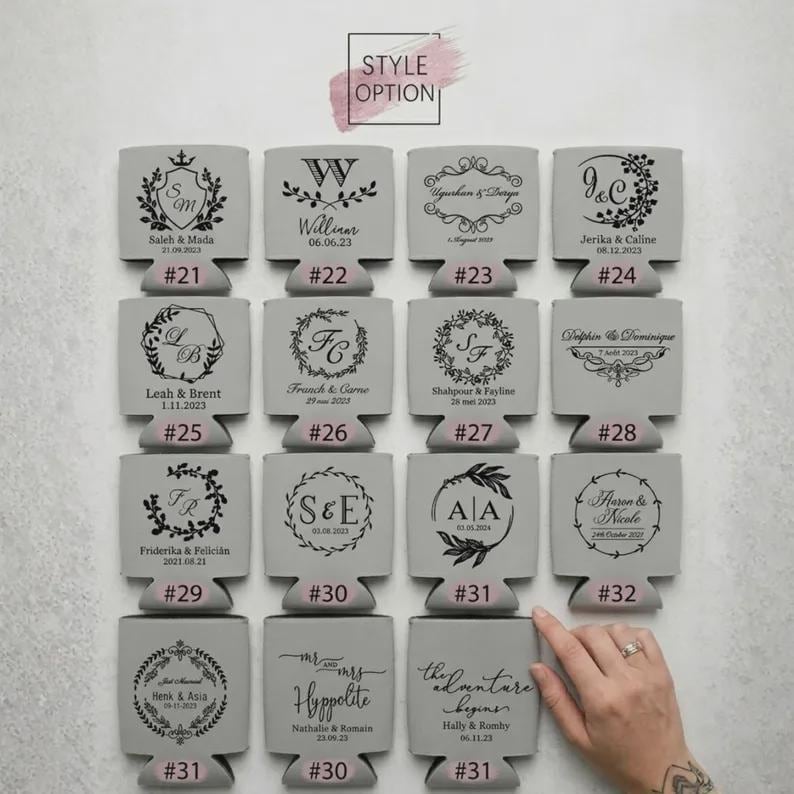 May include: A collection of sixteen light gray foam can coolers arranged in a four-by-four grid. Each cooler features a unique black printed design, including monograms, floral wreaths, and names with dates, labeled with numbers from 21 to 32.