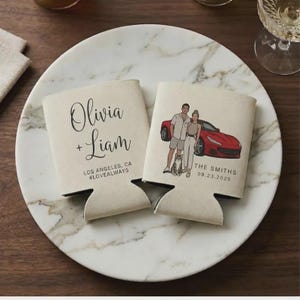 May include: Two off-white foam can coolers. One features the text Olivia + Liam, Los Angeles, CA, #LOVEALWAYS. The other displays a custom illustration of two people and a cat standing next to a red sports car, with The Smiths and 09.23.2025 printed below.