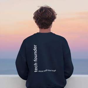 Può includere: Felpa blu navy con la scritta "tech founder" in verticale sulla schiena e "alone with the bugs" sotto. La persona è vista da dietro, con un tramonto sullo sfondo.
