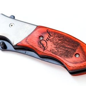May include: A red wood handled pocket knife with a silver blade. The handle is engraved with the word "Dad" and a fingerprint.
