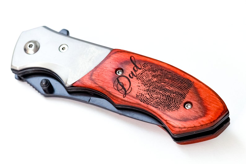 May include: A red wood handled pocket knife with a silver blade. The handle is engraved with the word "Dad" and a fingerprint.