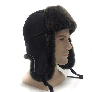 May include: A brown leather aviator hat with a faux fur earflap and chin strap. The hat is lined with faux fur and has a fold-down earflap.