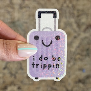 May include: A purple glitter sticker in the shape of a suitcase with a smiling face and the text "i do be trippin". The sticker has a white border and a retractable handle.
