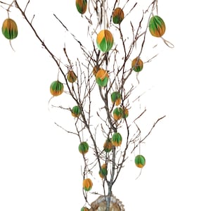Peut inclure: Un arbre de Pâques décoratif avec des branches brunes et des œufs en papier suspendus. Les œufs sont verts et orange, suspendus par des ficelles. L'arbre est dans un panier tressé.